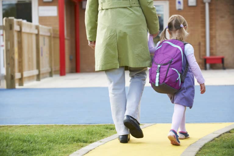 Mamma som følger liten jente til skolen og de går hånd i hånd.