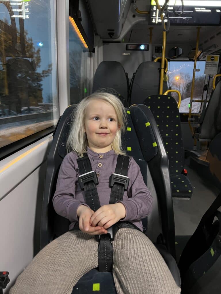 Bildet viser et barn som sitter i en bakovervendt intergrert barnesete i buss.