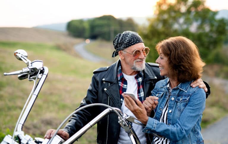 Et middelaldrende par som står ved siden av en motorsykkel.
