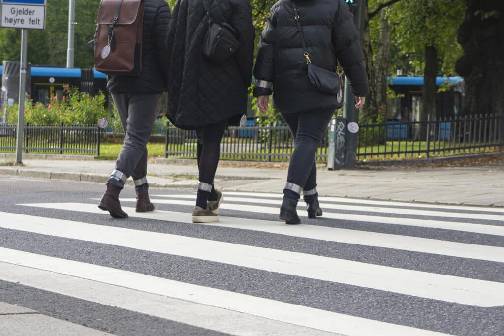 Tre personer som går over et gangfelt med slapwraprefleks på ankelen.