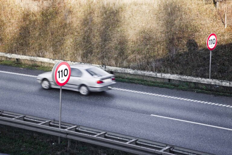 Bil i fart på vei med fartsgrenseskilt som viser 110 kilometer i timen som maks fart.