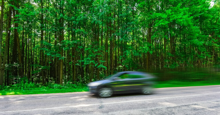 Bilde som illusterer bil i stor fart på vei med mye grønn skog i bakgrunnen.