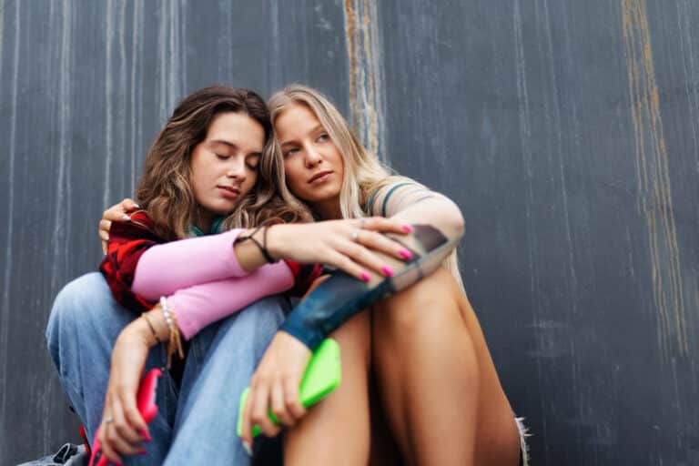 To jenter som sitter tett i tett og holder rundt hverandre.
