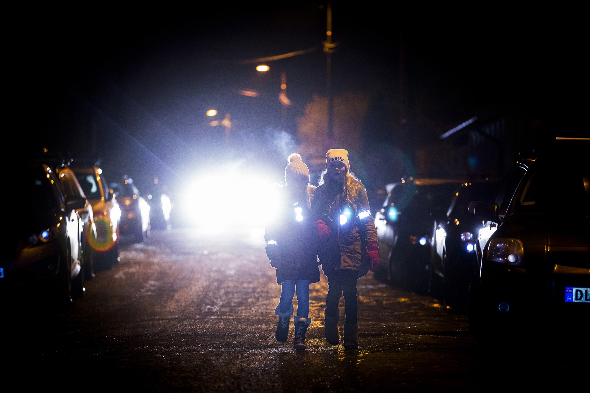 To jenter med reflekser på seg og en bil bak seg i mørket.