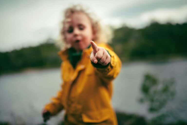 Liten gutt eller jente som peker mot fotografen.