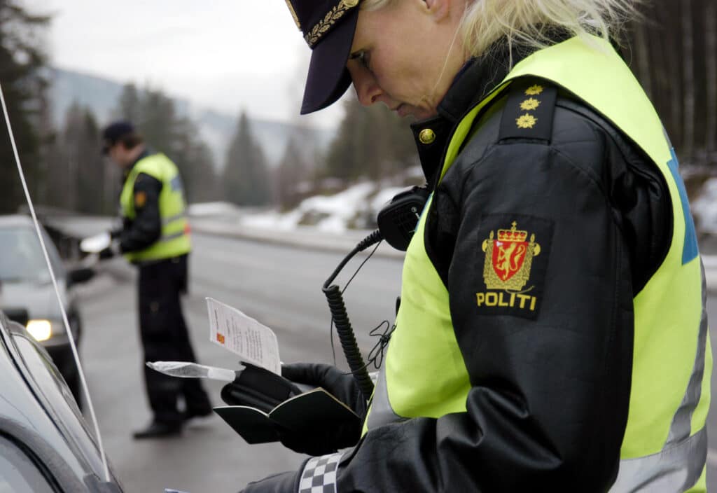Bilde av politi som gjør kontroll i en bil. Vi ser Politikvinne som ser på vognkortet til bilen.