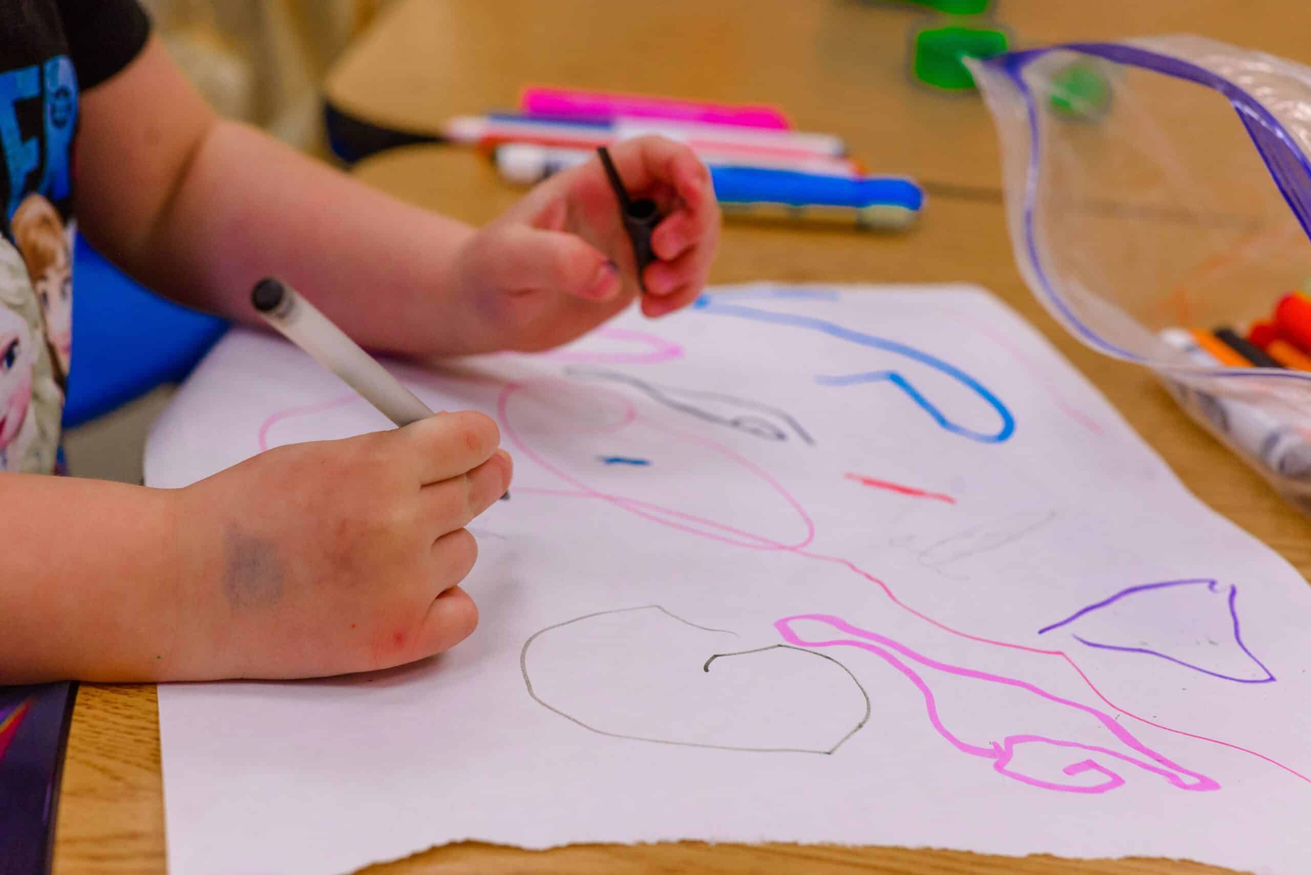 Barnehender som tegner på hvitt ark. Hendene har merker av farger.