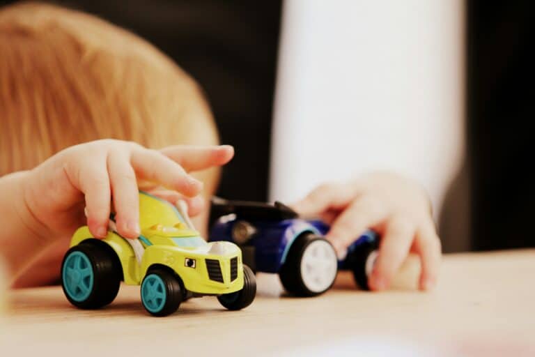 Et lite barn som leker med to biler på et bord. Vi ser bilene foran ansiktet.