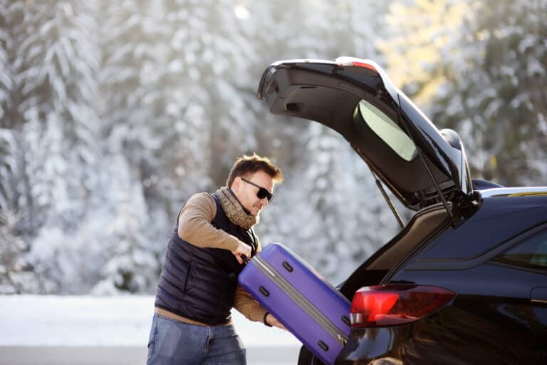 Mann putter en koffert i bagasjerommet på en bil.