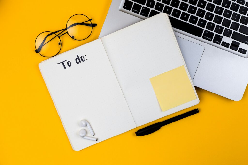 En åpen notatbok oppå et tastatur ved siden av noen briller. I boken står det "To do".
