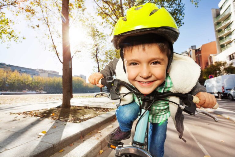 Bilde av gutt på sykkel med sykkelhjelm. Han smiler og er tett på kameralinsen.