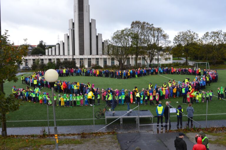 En stor gruppe mennesker som står i hjerteformasjon på en stor gressplen.